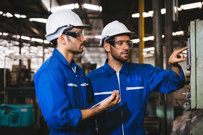 two men in blue jumpsuits performing conveyor system maintenance