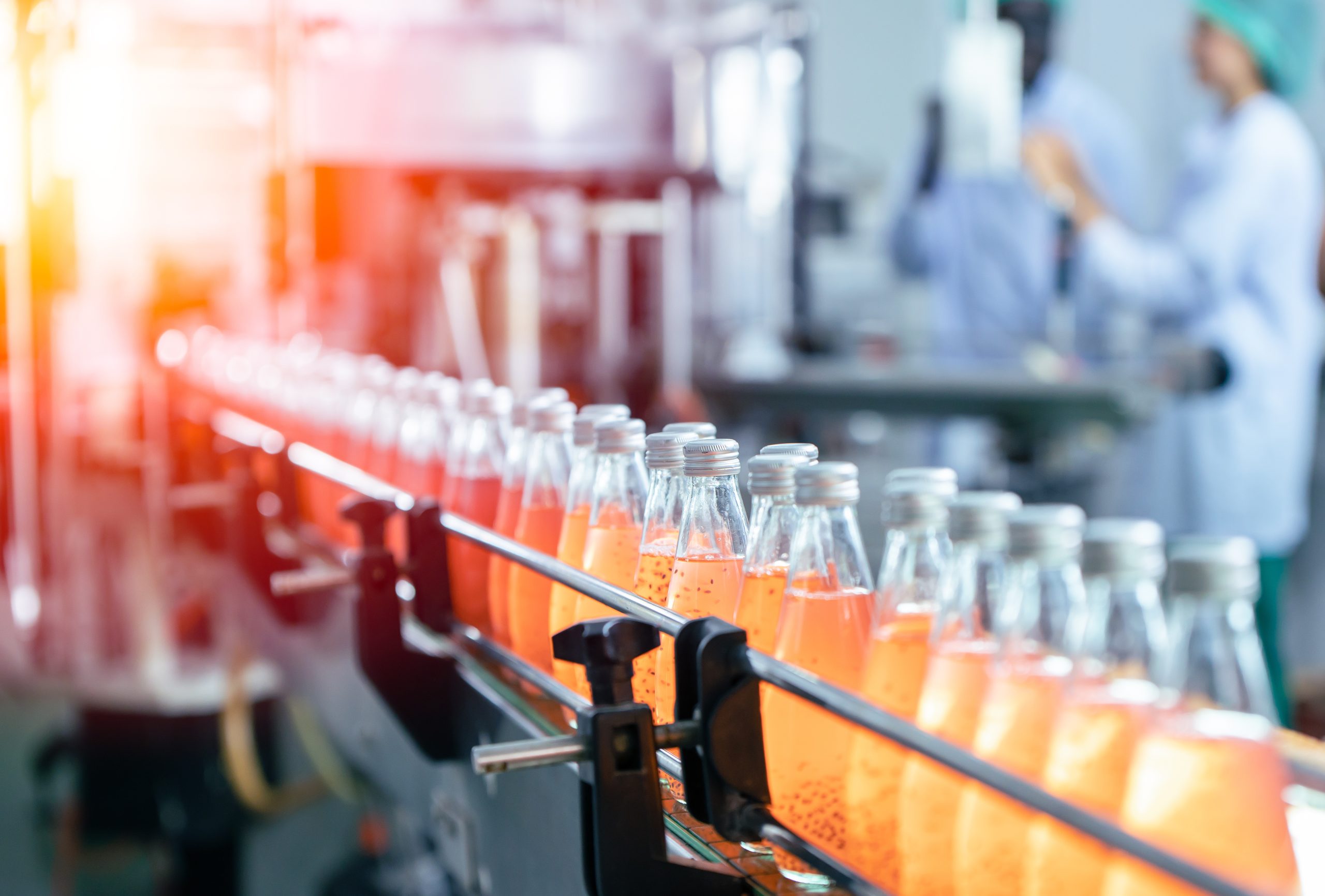 Bottles of orange soda in a straight line on a conveyor system in a manufacturing facility.