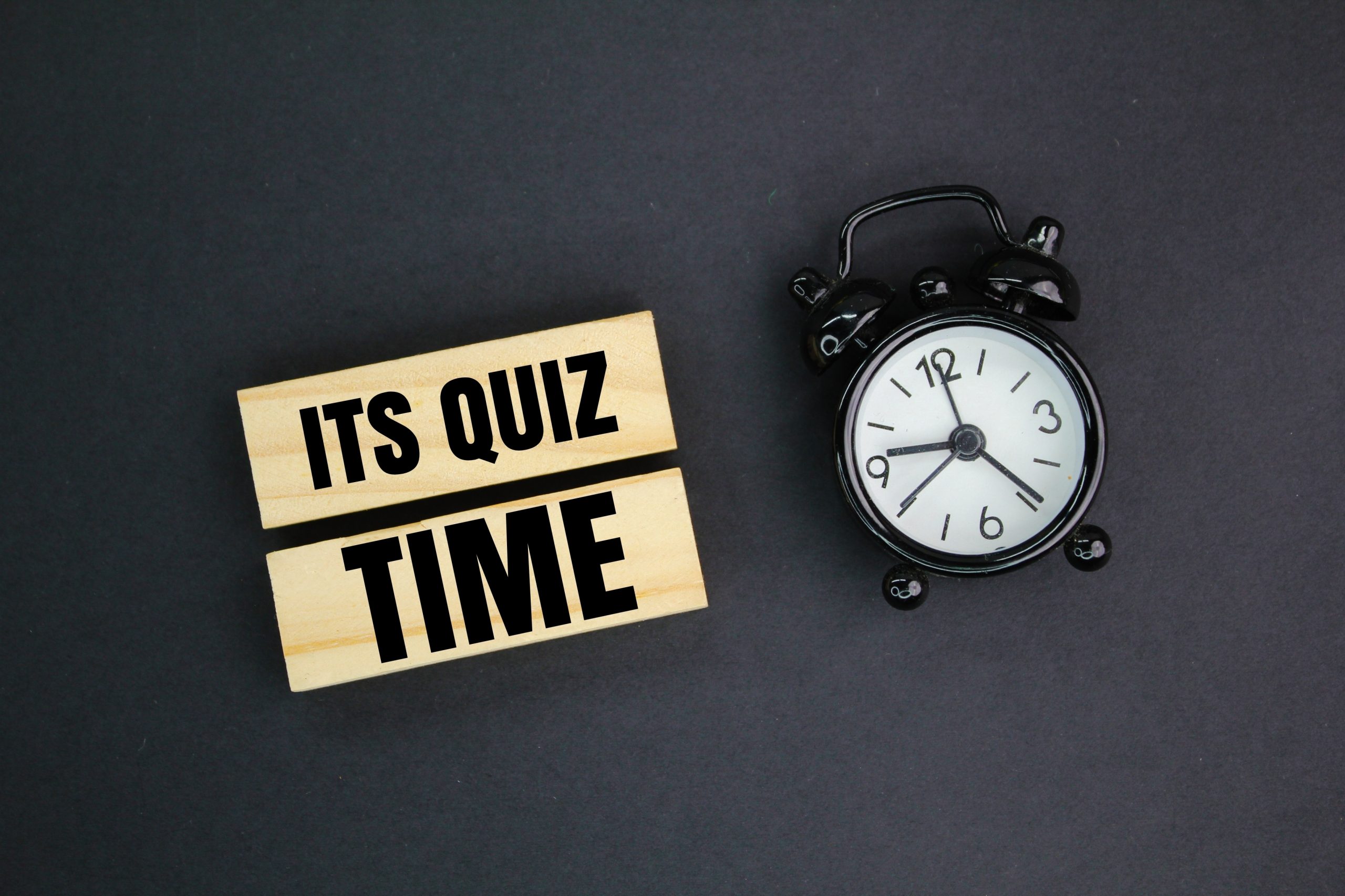 sign which says "It's Quiz Time" beside a clock against a black background