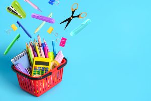 A red basket full of school supplies against a blue background